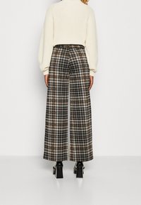 Breda byxor med rutig mönster i brun, svart och gräddvit, med en rutmönstring och hög midja, kombinerat med en gräddvit stickad topp.