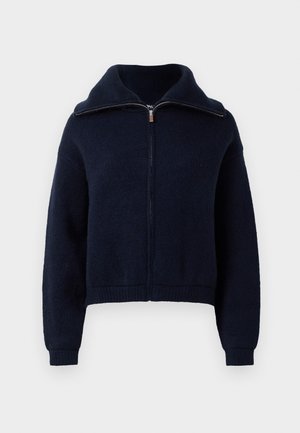 Marinblå zip-up-tröja med hög krage, långa ärmar och ribbade muddar och nederkant mot en vit bakgrund.
