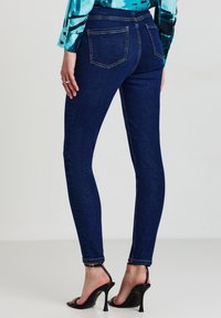 Jeans skinny blu in denim, con vita media, design a cinque tasche e texture liscia. Indossati con sandali neri con tacco.