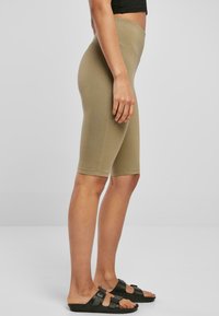 Khaki fietsbroek met een hoge taille, aansluitend ontwerp, gladde textuur en knielange snit, gecombineerd met zwarte slip-ons.