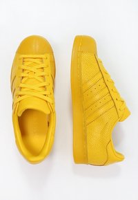 Zapatillas amarillas con un acabado de cuero suave y paneles laterales perforados. Presentan cordones planos, puntera redonda y suela de goma.