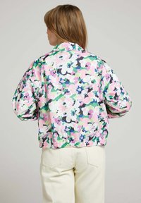 Veste bomber florale dans des teintes de rose, vert et noir ; tissu léger avec ourlet côtelé et poignets élastiques ; coupe ample avec manches bouffantes.