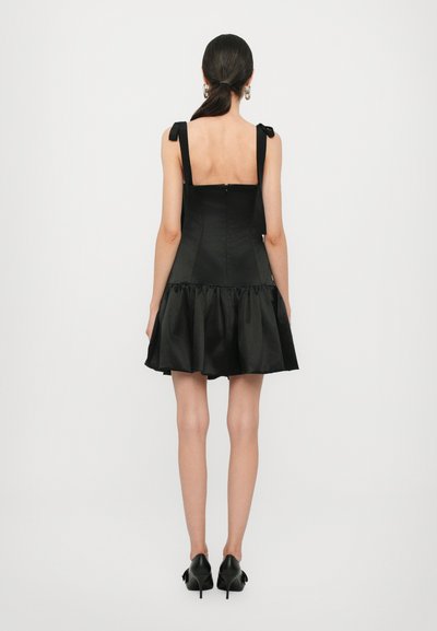 Vestido negro con un corpiño ajustado, tirantes de lazo y un dobladillo acampanado con volantes. Hecho de tela suave; cuenta con un cierre de cremallera en la parte posterior oculto.