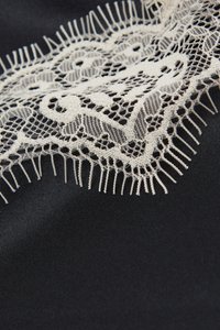 Tessuto nero con bordatura in pizzo bianco caratterizzato da motivi floreali, bordi smerlati e frange allungate, che creano un contrasto testurizzato.