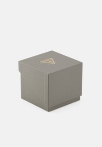 Boîte en carton gris avec une surface texturée. Présente un logo doré en forme de triangle sur le dessus. Design simple et carré.