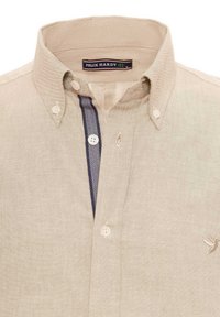 Camisa de botones beige con cuello, que presenta un patrón de cuadros azules en la tapeta y un pequeño logo bordado en el pecho.