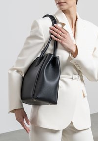 Black leather bucket bag with textured surface, rounded shape, and dual handles. Accents include gold feet on the base.