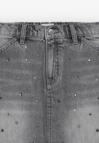 La falda de mezclilla gris presenta un diseño de cintura alta con adornos decorativos de tachuelas plateadas en formas de estrellas y círculos en la parte delantera y trasera.