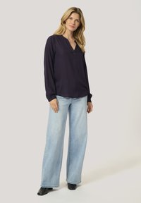 Navy blouse with a deep V-neck and long sleeves, paired with light blue wide-leg jeans. Material is smooth with a subtle drape. Black ankle boots.