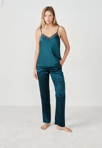 Camisola de satén color verde azulado con encaje en los bordes, combinada con pantalones de pijama a juego en color verde azulado con un patrón floral oscuro, diseño minimalista y corte holgado.