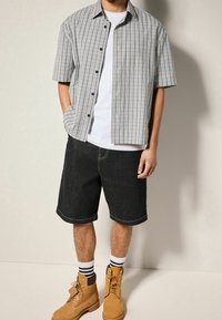 Shortsleevhe geruit shirt in blauw en wit, gecombineerd met zwarte denim shorts. Bruine veterschoenen met wit en zwart gestreepte sokken.