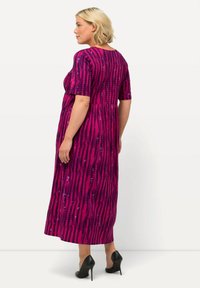 Różowa sukienka maxi w pionowe paski, z krótkimi rękawami i plisowanym tyłem. Posiada błyszczące akcenty i zwiewny krój, połączona z czarnymi obcasami.