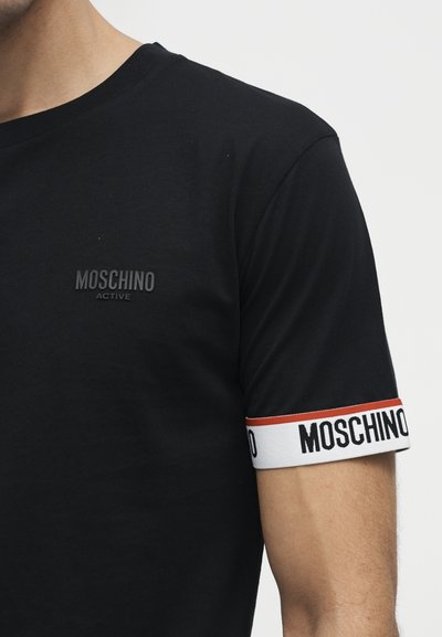 Chemise noire à manches courtes avec petit logo "Moschino Active" sur la poitrine et bord de manche blanc avec texte "Moschino" et bande rouge.