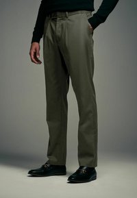 Pantalons en toile kaki en tissu lisse, avec une coupe droite, des passants de ceinture et des poches latérales, associés à des mocassins noirs.