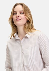 Button-up shirt in light fabric features vertical stripes in pale pink and cream, with a collar and two chest pockets. Soft texture.