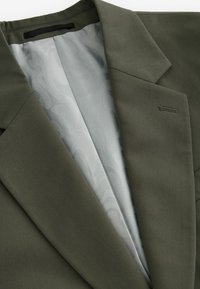 Olijfgroene blazer met inkepingen, voorzien van een gladde lichtgrijze patroonvoering en een detail van een enkele borstzak.