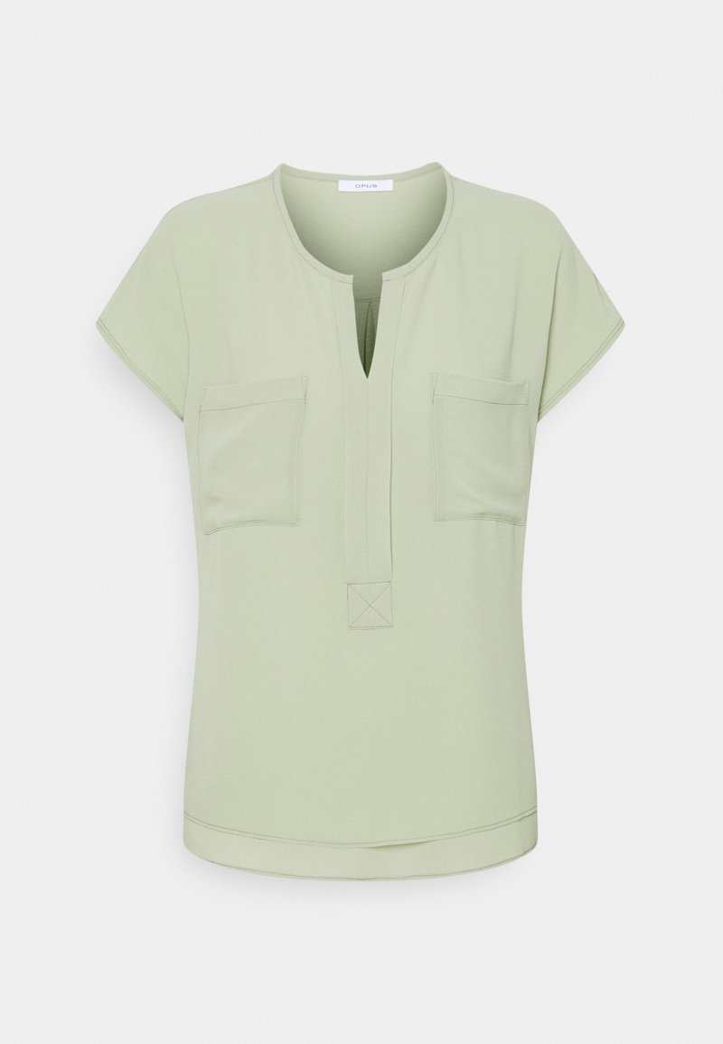 Top a maniche corte, di un verde chiaro, con scollatura a V, due tasche sul petto e un dettaglio cucito al centro. Texture morbida e design casual.