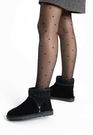 Botines de ante negros con un cuello de punto texturizado y cremallera lateral, combinados con medias negras con estampado de lunares.