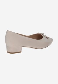 Scarpa beige con tacco basso in morbido camoscio, punta arrotondata e dettaglio decorativo a nodo sulla parte anteriore. Presenta un tacco a blocco stabile.
