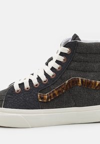 Baskets montantes en tissu noir avec un panneau latéral texturé, des lacets blancs et un accent distinctif en imprimé animal marron sur le côté.