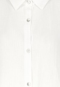White button-up shirt with a textured fabric, featuring a classic collar and five glossy buttons along the front.