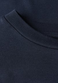 Primo piano di un collo di una maglietta di cotone blu navy con cuciture visibili e texture del colletto a costine.
