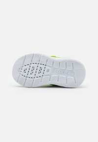 Suela de zapatilla blanca con patrón texturizado, soporte arch notable, agujeros de drenaje y acentos verdes cerca del talón.