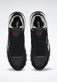 Baskets Reebok Classic noir et blanc avec lacets noirs, logo rouge et gris sur la languette, et détail jaune au col du talon, vues de dessus.