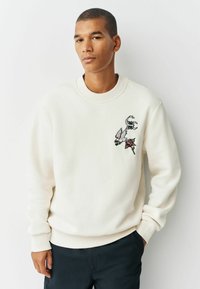 Cream-colored sweatshirt made of soft fabric, featuring embroidered graphic designs of a scorpion, rose, and bird on the left chest area.