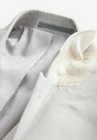 Col de veste gris clair avec une doublure intérieure douce et texturée et un motif géométrique subtil sur un tissu intérieur lisse.