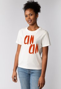 Witte katoenen T-shirt met dikke rode "CIN" tekst. Korte mouwen en ronde hals, in combinatie met lichtblauwe denim jeans.