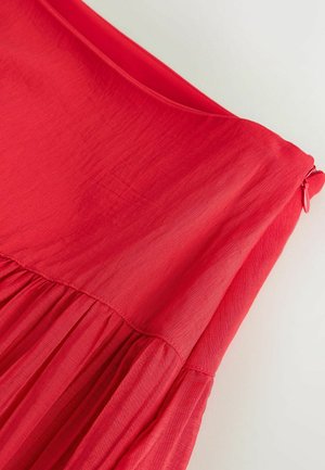 Punase kanga kleidi lähedalt vaadatuna, kus vöö all on kortsudega õmblus ja külje peal punase tõmblukuga tõmmitsa