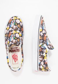 Baskets slip-on Vans avec un tissu noir orné de personnages colorés du dessin animé Peanuts, semelle en caoutchouc blanc et contour noir contrastant.