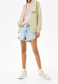 Zrzucenie beżowej kurtki, różowy sweter w sploty, zniszczone dżinsowe szorty oraz beżowe trampki z różowymi akcentami.