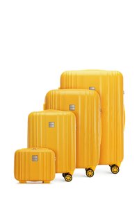 Vier gele harde koffers van verschillende maten, met ribbeltextuur, gladde oppervlakte en spinnerwielen. Elke koffer heeft een merklogo op een zilveren plaat.