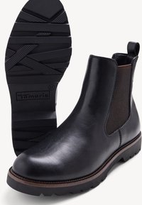 Stivaletti Chelsea in pelle nera con pannelli elasticizzati, suola in gomma testurizzata e un accento marrone attorno alla base. Marchio visibile sulla suola.