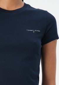 Maglietta in cotone blu navy con scollo rotondo e maniche corte. Presenta il logo bianco "TOMMY JEANS" nella zona sinistra del petto.