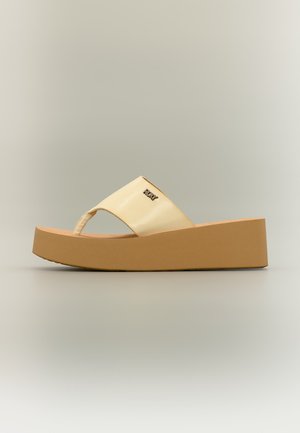 Beež värvi kiilkingadega sandaal paksu tallaga, avatud varvastega, laia rihmaga ja väikese metallist logoga rihmal.