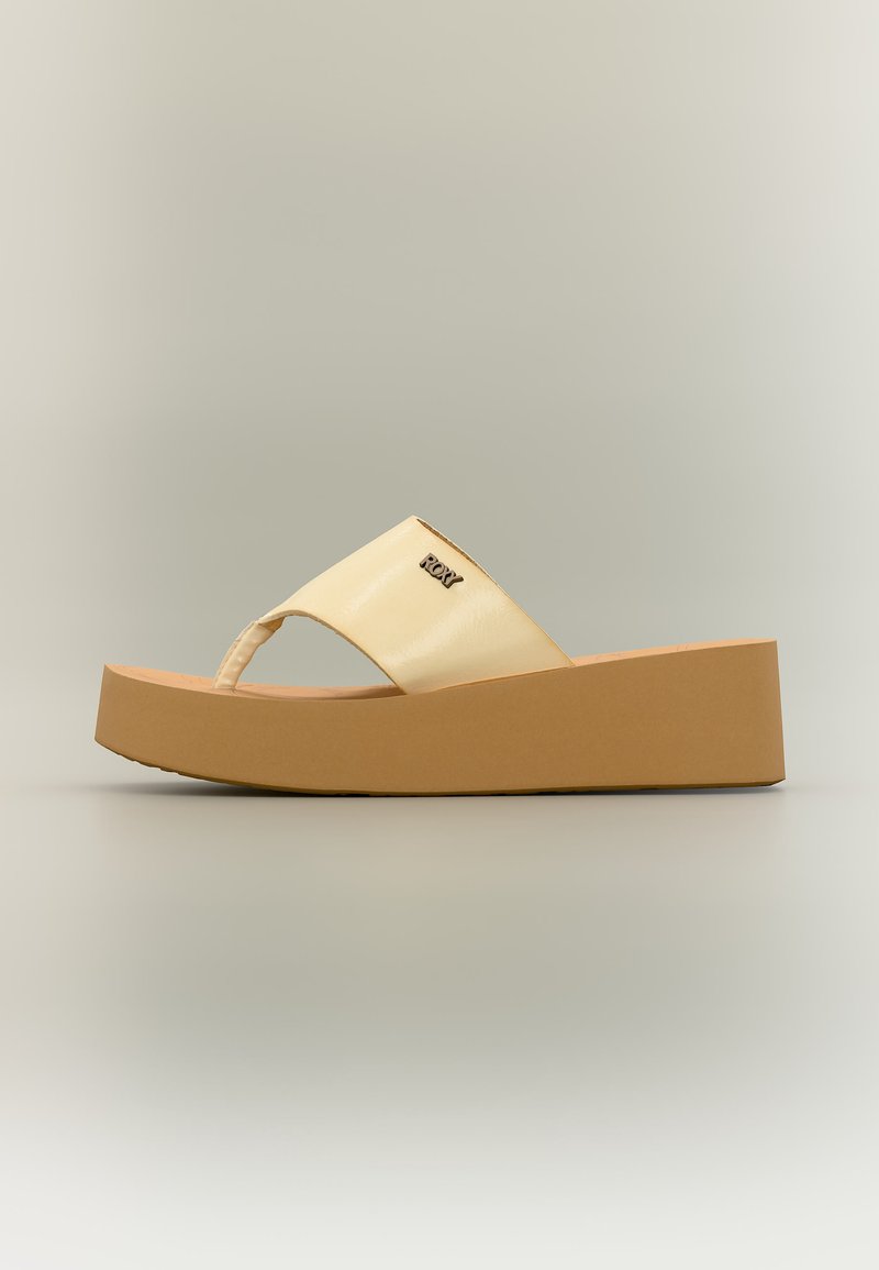 Sandale compensée beige avec semelle épaisse, bout ouvert, large bride et petit logo métallique sur la bride.