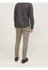 Vue de dos d'un homme portant une chemise à manches longues rayée bleu marine et beige, complétée par des chaussures marron. La chemise présente des rayures verticales.