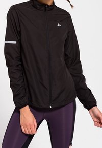 Czarna lekka kurtka z przednim suwakiem, wysokim kołnierzem oraz odblaskowym paskiem na rękawie. Gładka faktura i sportowy krój.