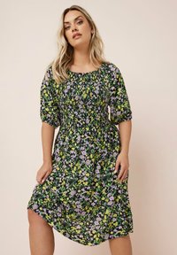 Kukallinen mekko, jossa on musta tausta ja purppuravia sekä keltaisia kukkia, lyhyet puhallettut hihat ja vyötäröstä kireä, ulottuen juuri polven ylle.