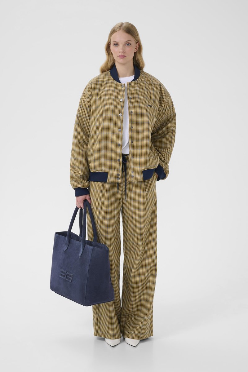 Yellow and navy checked bomber jacket, white top, matching checked pants, and a blue suede tote bag with embossed detail. White shoes.