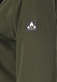 Olijfgroene jas met een gladde textuur en een zwart vierkant patch met een wit logo dat drie gestileerde bergvormen toont.