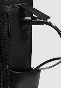 Zwarte leren rugzakinterieur met een USB-laadpoort, gestructureerde stof en een ritsvak met een gevlochten kabel.