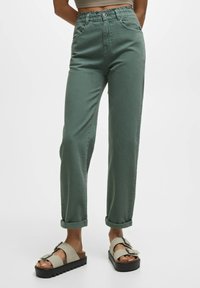 Pantalon en coton vert à coupe décontractée, doté d'une taille à cordon, d'ourlets roulés et de poches latérales. Associé à des sandales beige avec une semelle noire.