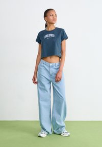 Cropped navy t-shirt with "Nike Sports" logo, paired with loose light blue jeans and white sneakers with grey accents.