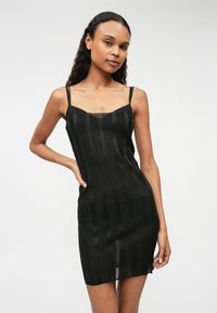 Musta neulemekko ohuilla olkaimilla, jossa on pystyraitoja ja läpinäkyviä osioita, juuri polvien ylle ulottuva malli.