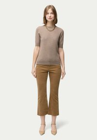 Ljusbrun stickad tröja med korta ärmar, tillsammans med kordflätsbyxor med utsvängd passform. Beige klackar och ett tjockt guldkedjehalsband fulländar looken.