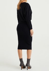 Svart stickad klänning med långa ärmar, figursydd silhuett, ribbat mönster och knälång nederkant. Matchad med grå högklackade ankelstövlar.